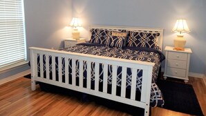 A bedroom with a white crib, a bed with patterned bedding, two bedside tables with lamps, and a window with blinds.