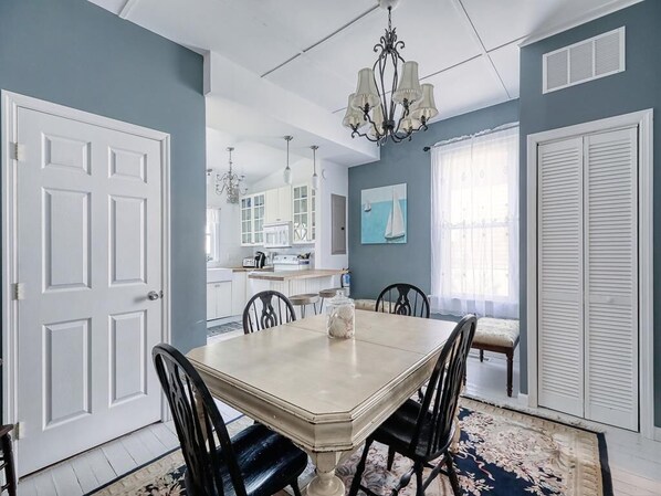 A dining room with a large table, chairs, and a chandelier. There is a kitchen in the background with cabinets and a window. - Walk to Shopping&Restaurants. A few blocks to the beach. (Cape May)