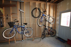A garage with two bicycles, a tire hanging on the wall, and a door with a window.