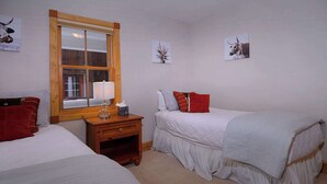 A bedroom with two beds, a wooden nightstand, a window, and wall art.