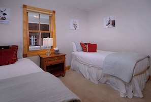Ein Schlafzimmer mit zwei Betten, einem Nachttisch aus Holz, einem Fenster und Wandbildern.