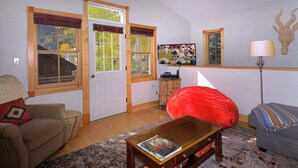 A living room with a sofa, a red bean bag, a coffee table, a television, and a door leading outside.