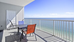 Un balcon avec une table et des chaises, une porte blanche et une vue sur l’océan.