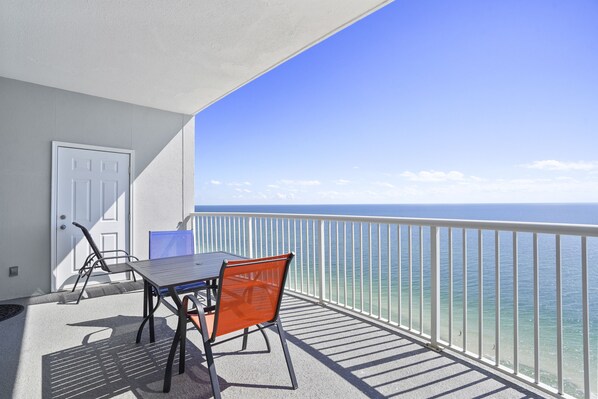 Un balcon avec une table et des chaises, une porte blanche et une vue sur l’océan.