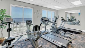 Une salle de sport équipée de tapis de course, de vélos elliptiques et d’un vélo d’appartement, de grandes fenêtres offrant une vue sur l’océan et d’un plafond doté d’un éclairage encastré.