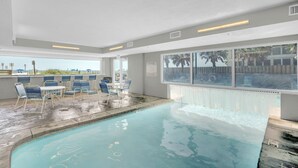 Une piscine intérieure à l’eau d’un bleu cristallin, entourée de chaises longues et d’une table.