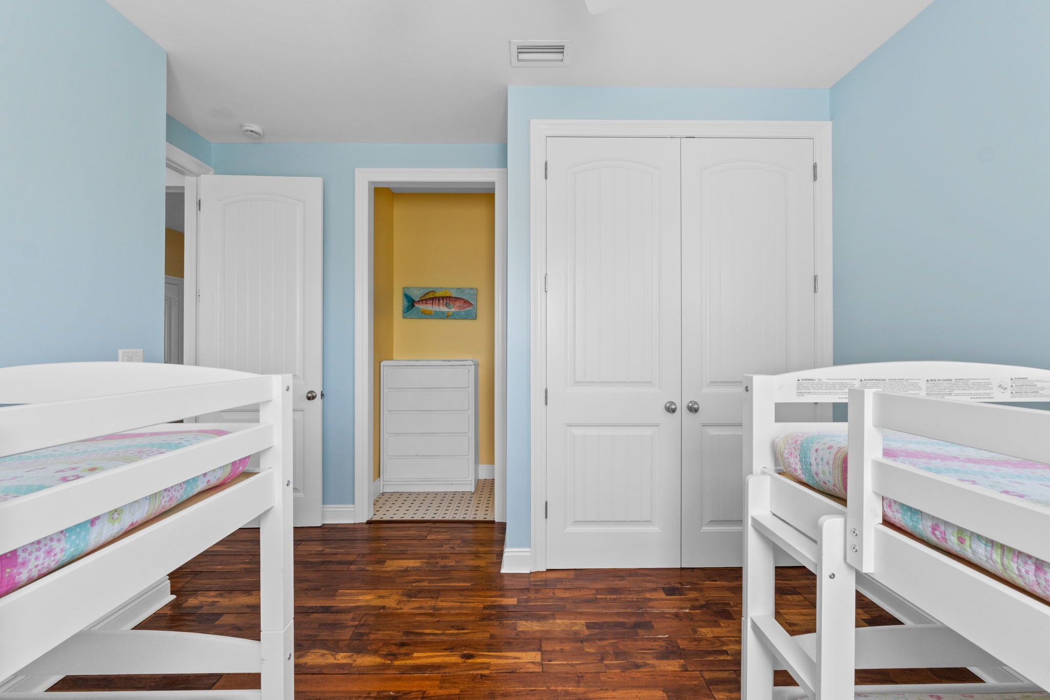 A bedroom with two bunk beds, a door leading to another room, and a painting on the wall.