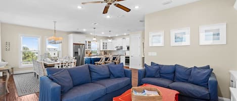 A spacious living room with a large blue sofa set, a red coffee table, and a ceiling fan.