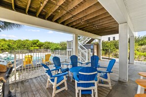 Un espace extérieur abrité comprenant une piscine, des fauteuils Adirondack bleus et jaunes, et un barbecue.