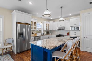 A modern kitchen with white cabinets, stainless steel appliances, a blue island, and wicker chairs.
