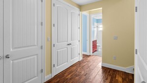Un couloir avec des portes blanches, un plancher en bois et une salle de bain visible au fond.