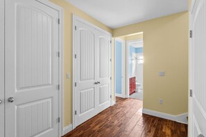Un couloir avec des portes blanches, un plancher en bois et une salle de bain visible au fond.