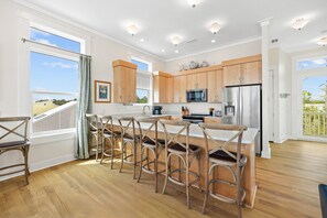 A modern kitchen with wooden cabinets, a stainless steel refrigerator, and a bar area with stools. - Southern Exposure: 4th of July week available as a Friday or Saturday check in! (Port St. Joe)