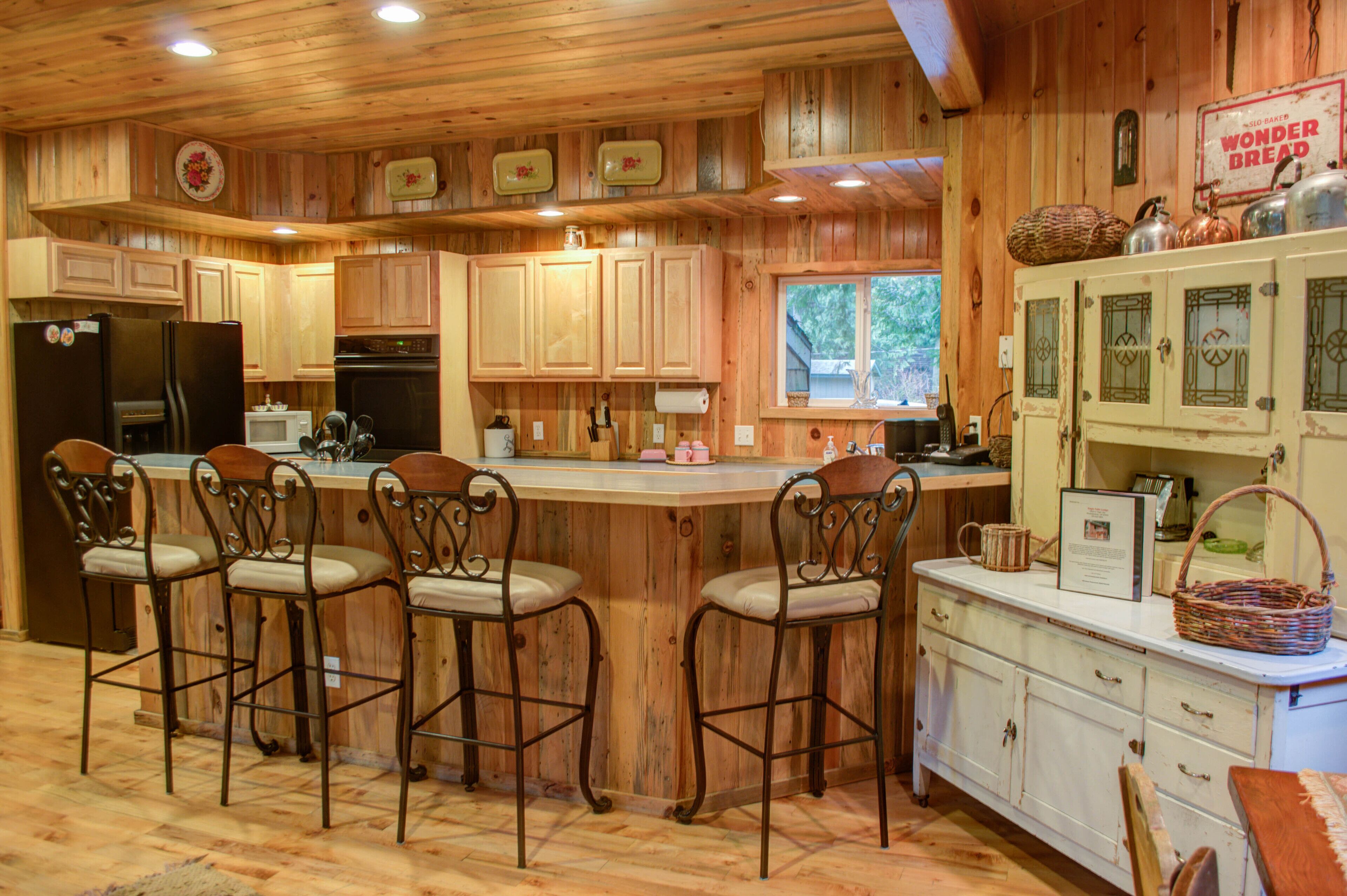 Une cuisine rustique aménagée dans une cabane en bois, avec un îlot central, des tabourets de bar et des meubles de style vintage.