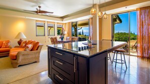 A modern kitchen with a central island, dining area with chairs, and a view of the outdoors. - Celebrated Villa, stylish and stunning golf views (Lahaina)