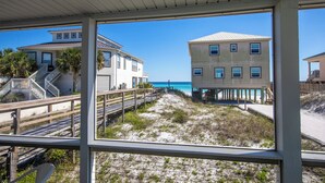 Ein direkt am Strand gelegenes Anwesen mit einer Holzterrasse, einer Treppe, die zu einem Balkon führt, und Meerblick.