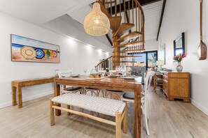 A spacious dining area with a wooden table set for six, a woven bench, and a spiral staircase in the background.