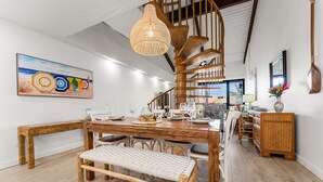 Un comedor amplio con una mesa de madera dispuesta para seis personas, un banco tejido y una escalera de caracol al fondo.