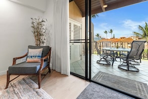 A room with a chair, a potted plant, and a view of an outdoor patio with a table and chairs.