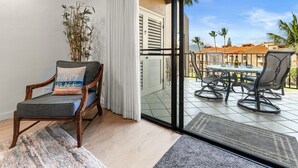 Una habitación con una silla, una planta en maceta y vistas a un patio al aire libre con mesa y sillas.