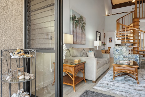 A living room with a sofa, a glass coffee table, a wicker chair, and a staircase.