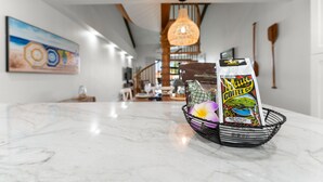 Una encimera de mármol con una cesta de alambre negra que contiene un paquete de café Maui y un cuenco decorativo.