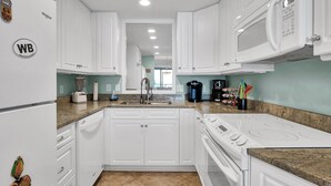 A modern kitchen with white cabinets, a built-in stove, a microwave, and a sink.
