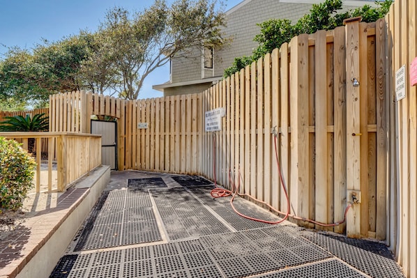 A pool area with a wooden fence, a metal grate floor, and a sign indicating a poolside shower. - Station One - 6J Beach Haven- Oceanfront condo with pool, tennis, beach (Wrightsville Beach)