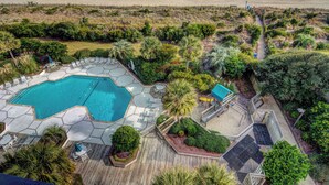 An aerial view of a resort with a swimming pool, deck chairs, and a beach view.
