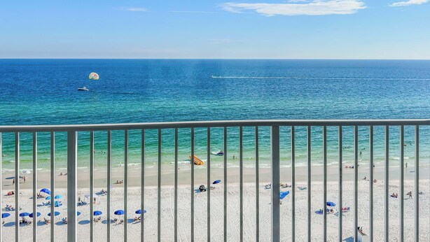 Une vue sur la plage depuis un balcon doté d’une balustrade, avec une mer d’un bleu limpide et des parasols de plage.