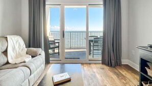Un salon avec un canapé, une table basse sur laquelle se trouve un livre, et une vue sur la mer par une porte coulissante.