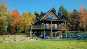Une cabane en bois dotée d’un balcon, entourée d’un feuillage automnal et d’une pelouse bien entretenue.