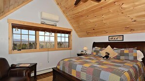 Une chambre à coucher avec un grand lit, un plafond en bois, une fenêtre donnant sur un beau paysage et une table de chevet avec une lampe.