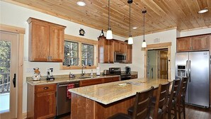 Une cuisine moderne avec des meubles en bois, des appareils en acier inoxydable et un grand îlot central doté de tabourets de bar.
