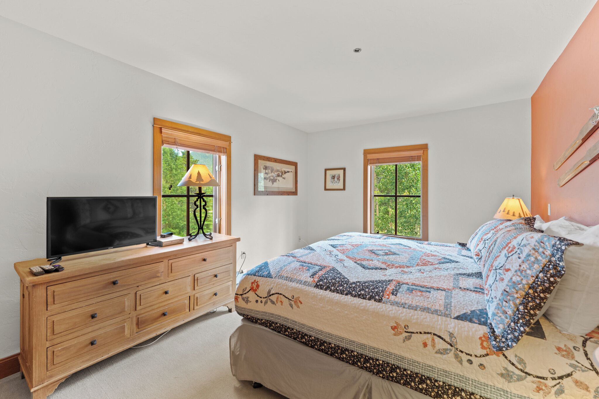 Un dormitorio con cama, tocador, televisor y dos ventanas.