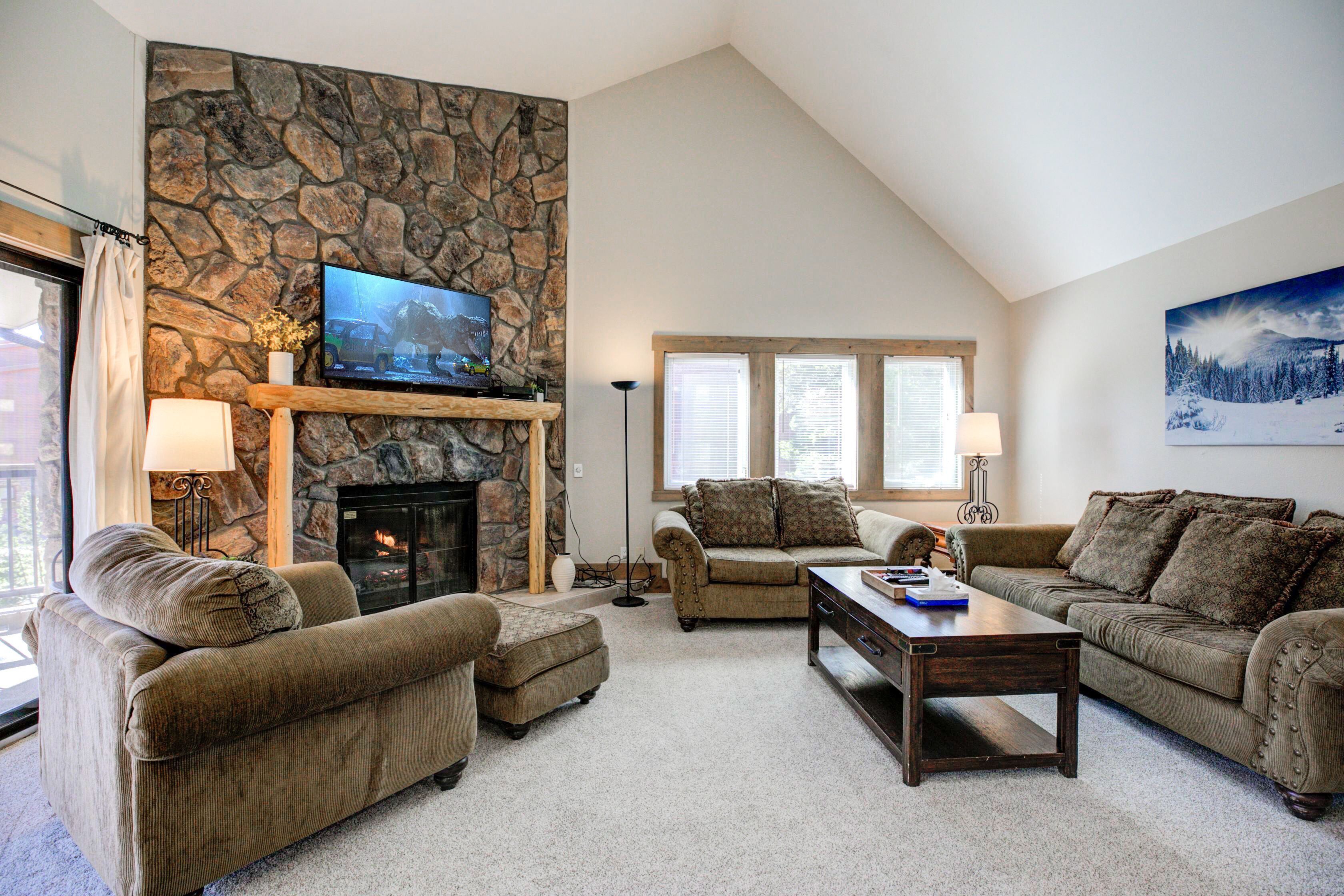 A living room with a stone fireplace, two sofas, a coffee table, and a television mounted on the wall.