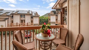 A balcony with wicker chairs and a table, overlooking neighboring buildings and a red car.