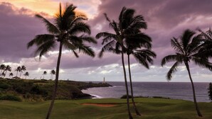 A golf course with palm trees and a lighthouse in the background.