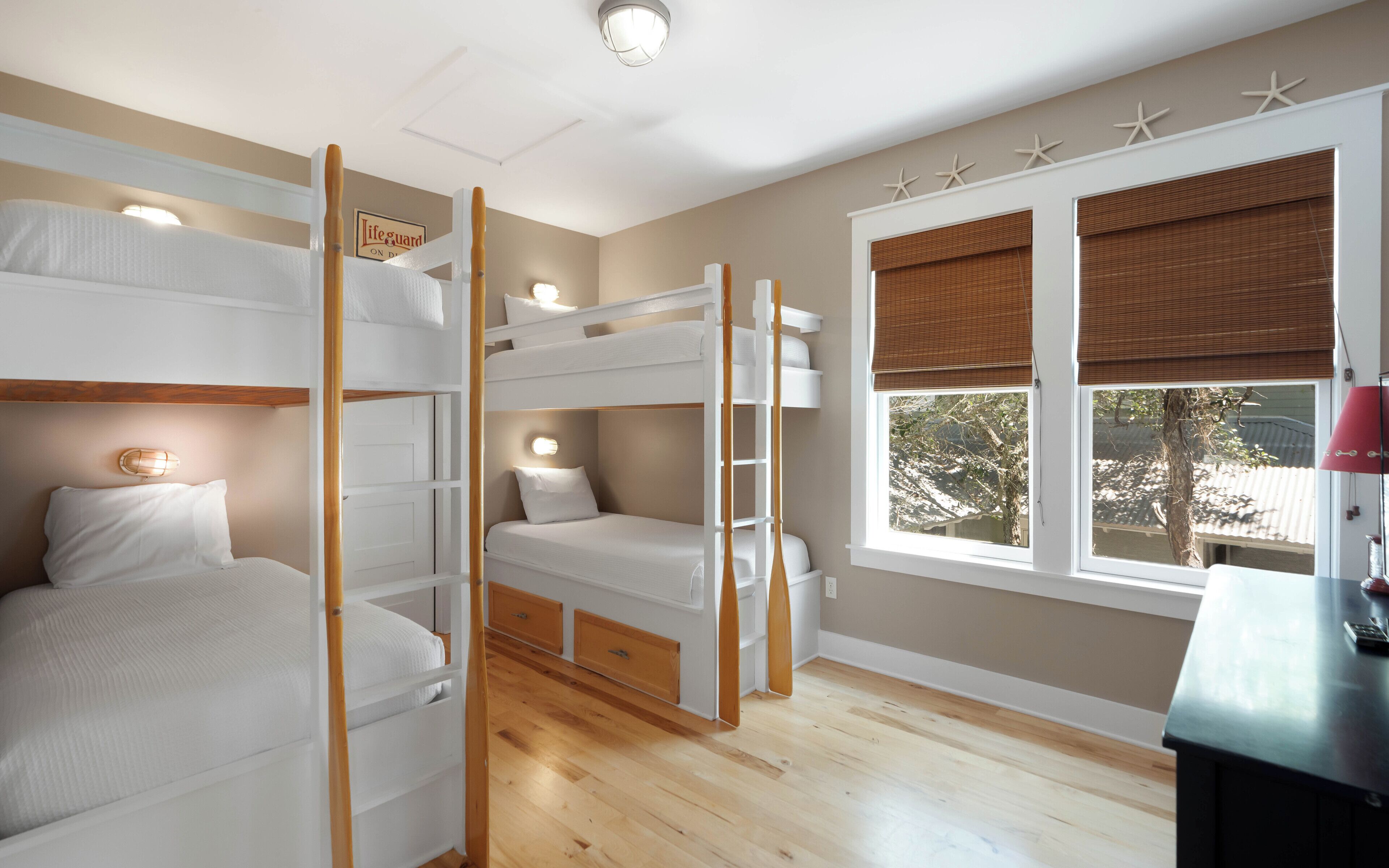 A room with bunk beds, a desk, a window with blinds, and a sign on the wall.
