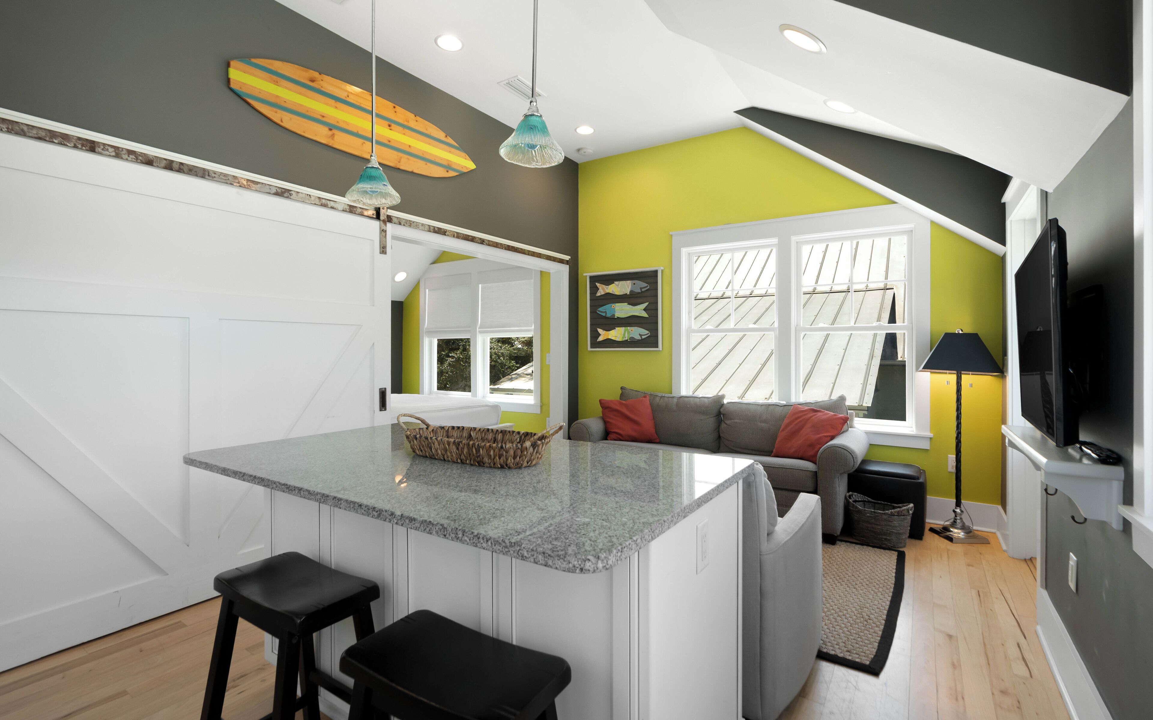 A modern kitchen with a central island, bar stools, a dining area with a sofa, and a TV.