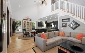 A spacious living area with a gray sectional sofa, a dining table with chairs, and a kitchen in the background. - Sandy Oar - Camp WaterColor Home + Carriage House, Fire Pit,  5 Bikes (Santa Rosa Beach)