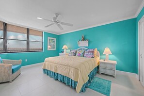 A bedroom with a bed, two bedside tables, a ceiling fan, a window with blinds, and a teal wall.