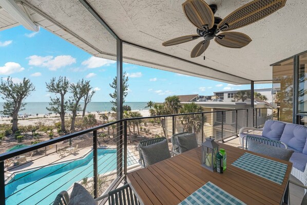 A balcony with a view of a beach, a pool, and a table with outdoor furniture.
