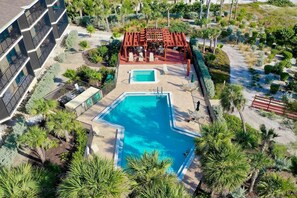 An aerial view of a resort with a large rectangular pool, a covered seating area, and lush landscaping.