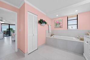 A modern bathroom with a large bathtub, a white vanity, and a pink accent wall.