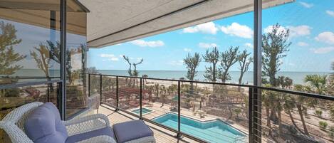 Un balcón con sillas de mimbre, una piscina y vista a una playa y al océano.