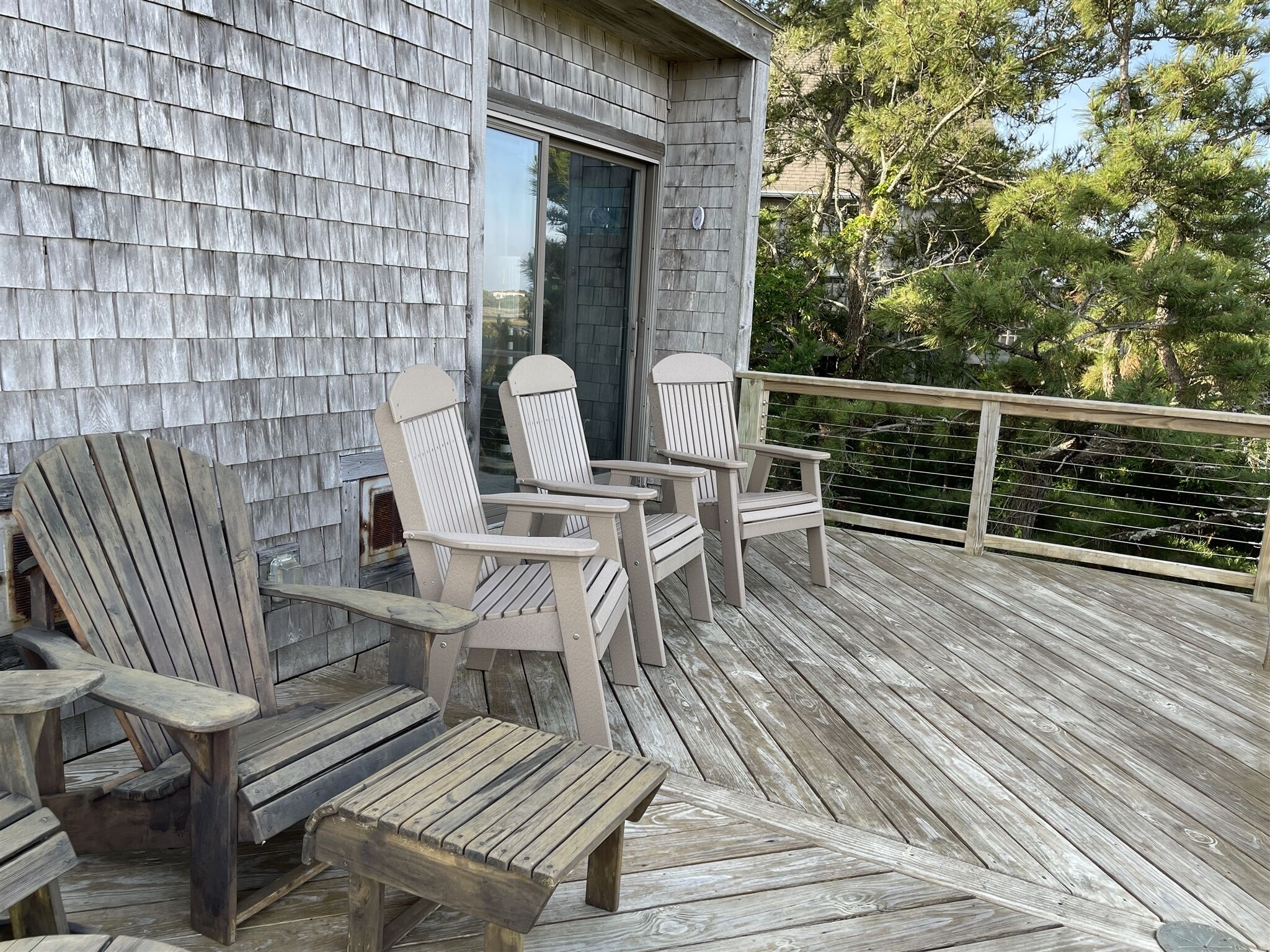 Een houten terras met Adirondack-stoelen en een kleine tafel.