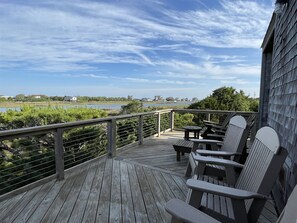 A wooden deck with Adirondack chairs overlooking a body of water and distant buildings. - Will's Hideaway Quiet, Secluded and Pet Friendly! (Hatteras)