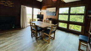 Un intérieur en bois comprenant une table à manger, des chaises, un téléviseur et de grandes fenêtres.