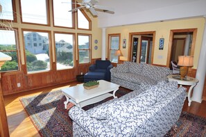 A spacious living room with large windows, a ceiling fan, and a view of neighboring houses. - Silver Creek: Semi-Oceanfront, Private Pool, Hot Tub (Southern Shores)
